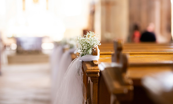 decorated wooden church pews with arrangement of baby breath flowers and white tulle draping for a wedding featuring six floral accents